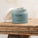 An open jar of Tropic Body Care Foot Smooth Enzymatic Scrub with a white lid resting to the side, placed on a rustic wooden surface.